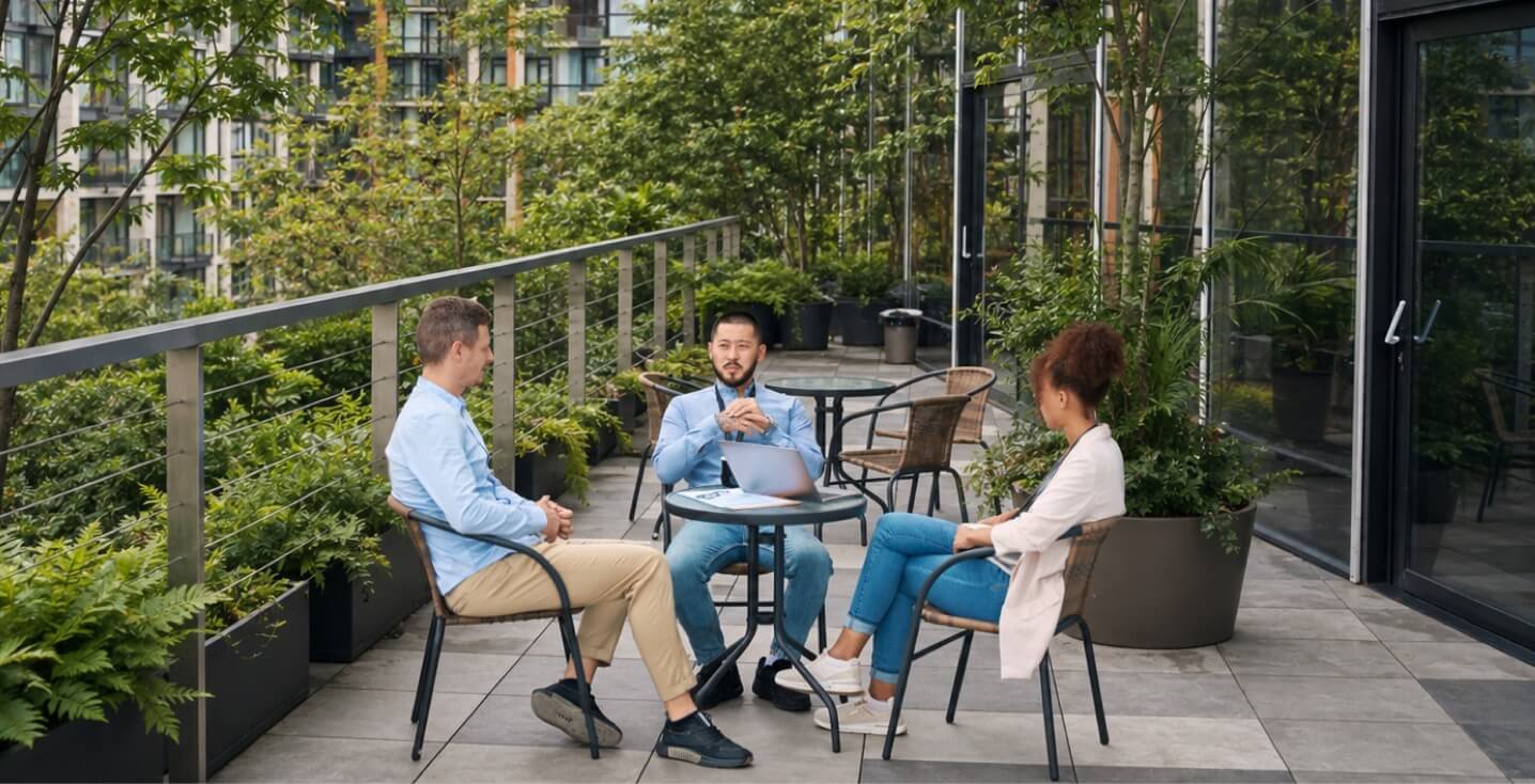 Coworkers sitting chatting on a skyskaper balcony surrounded by trees and ferns.