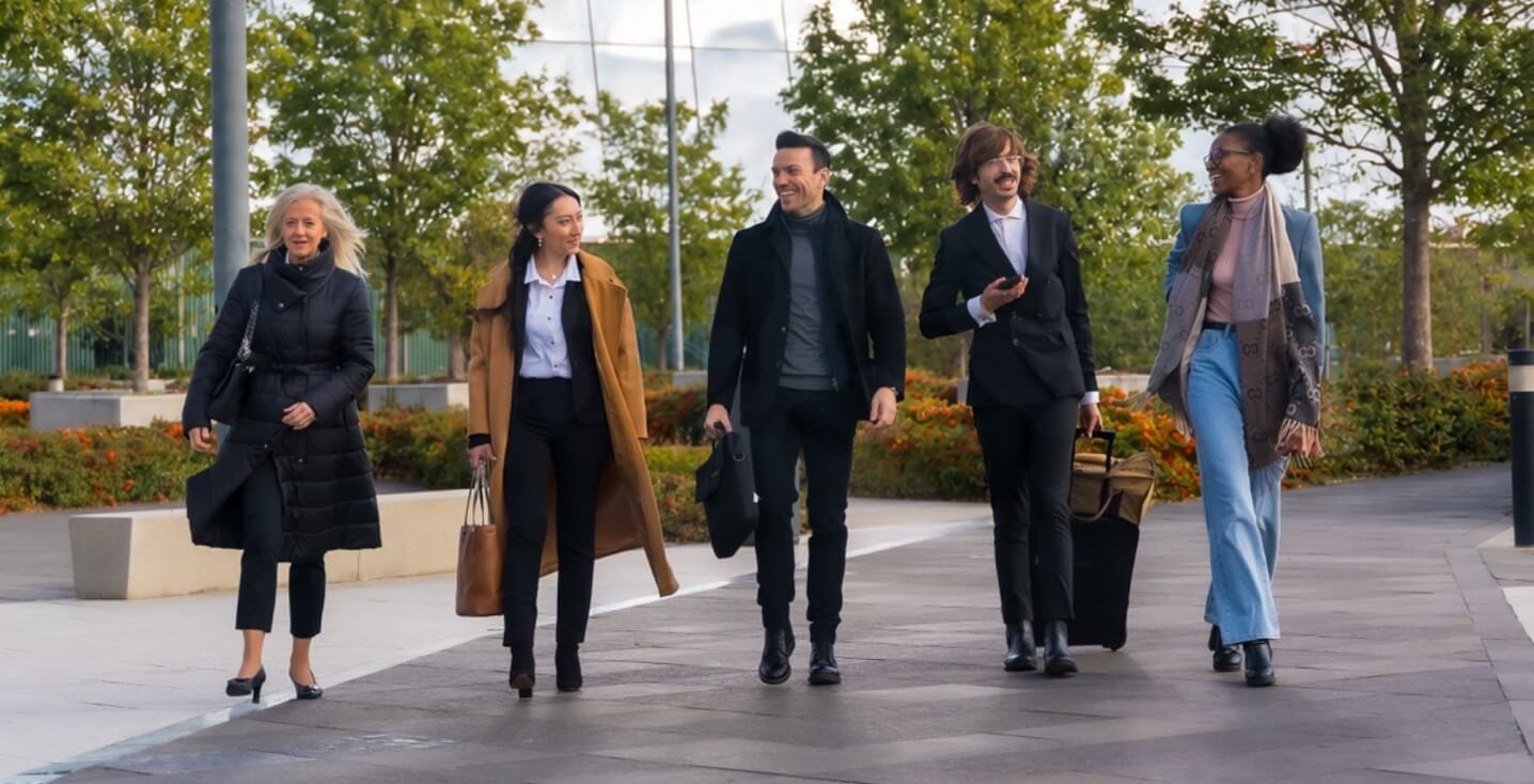 Coworkers walking through an office park surrounded by lush trees.